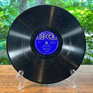 May include: A black vinyl record with a blue label. The label says "Decca" and features the song "Amapola (Pretty Little Pepper)" by Jimmy Dorsey and His Orchestra. The record number is 3029 A.