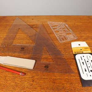 May include: A collection of drafting tools including two clear plastic triangles, a stencil, an erasing shield, and a red pencil. The tools are arranged on a wooden surface, ideal for architectural or engineering projects.