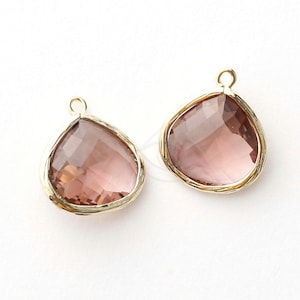 May include: Two gold-toned pendant charms with a teardrop-shaped, faceted, light pink glass stone.