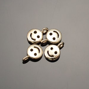 Puede incluir: Cuatro abalorios de metal de color dorado en forma de caritas sonrientes con un bucle en la parte superior para sujetarlos a un collar o pulsera.