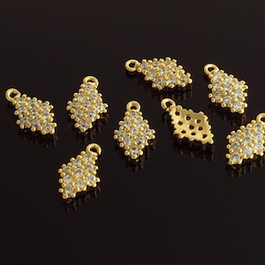 Puede incluir: Una colección de ocho dijes de metal dorado con detalles de diamantes de imitación transparentes. Los dijes tienen forma de diamante y tienen un bucle en la parte superior para sujetarlos a joyas.