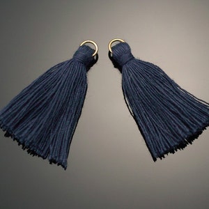 Puede incluir: Dos borlas de acabado azul oscuro con anillos de metal dorado.