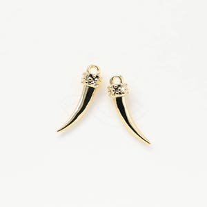 May include: Two gold-toned metal charms shaped like a curved tusk with a textured top.