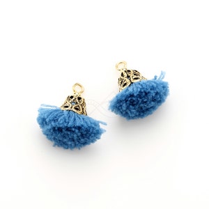 Könnte beinhalten: Zwei blaue Quasten-Ornamente mit goldenen Metallkappen. Die Quasten bestehen aus weichem, flauschigem Garn und die Kappen haben ein dekoratives, filigranes Design.