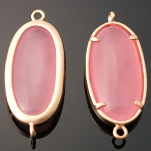 May include: Two oval-shaped pink glass cabochons with gold-tone metal settings and loops for hanging.