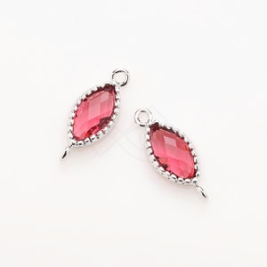 May include: Two silver-toned pendant charms with a red faceted glass marquise shape. Each charm has a small loop at the top and a small loop at the bottom.