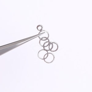 May include: Silver-toned metal chain with multiple interconnected rings, held by tweezers against a white background.