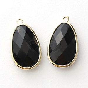 May include: Two black faceted teardrop-shaped glass charms with gold-toned metal frames and loops.