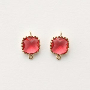 May include: Two gold-toned square-shaped pendant charms with a red crystal in the center. The charms have a decorative border and a loop at the top.