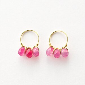 May include: A pair of gold hoop earrings with three pink chalcedony stones dangling from each hoop.