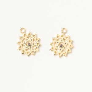 Pode incluir: Dois pingentes de metal dourado em forma de mandala com um pequeno strass transparente no centro.