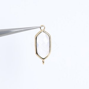 May include: Gold-toned pendant with a clear faceted gemstone in a hexagonal shape. The pendant has a loop at the top for attaching to a chain or cord.
