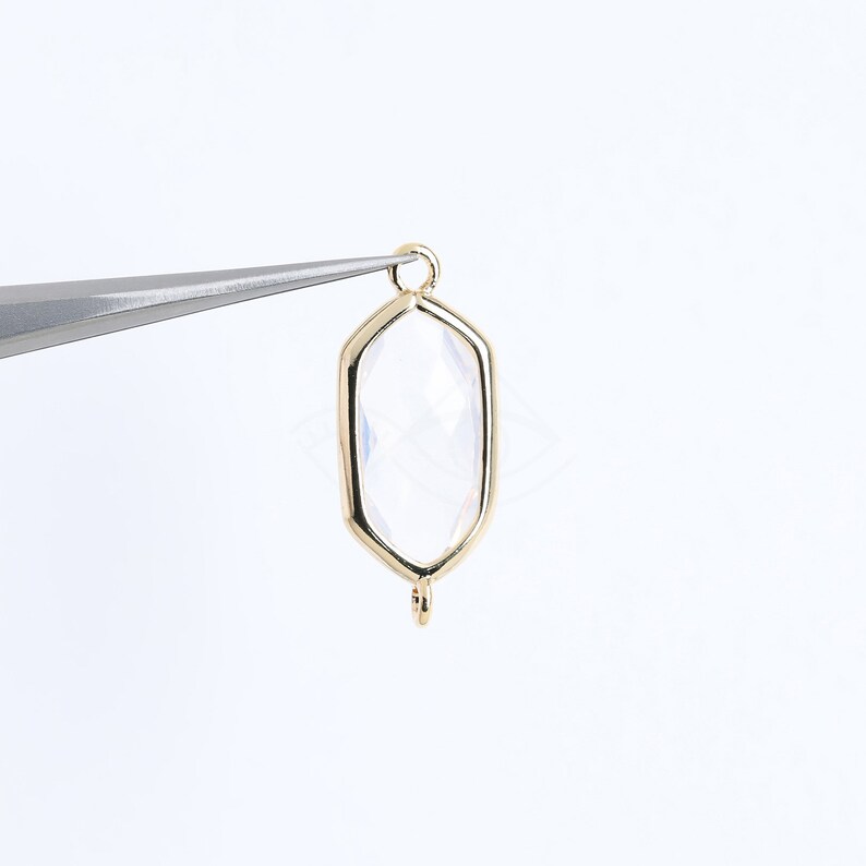 May include: Gold-toned pendant with a clear faceted gemstone in a hexagonal shape. The pendant has a loop at the top for attaching to a chain or cord.