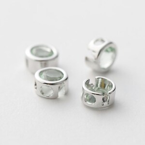 May include: Four silver-toned metal bead caps with clear green glass stones. The bead caps have a round shape and a hole in the center.