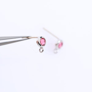 以下が含まれることがあります： 小さなピンクの宝石とジャンプリングが付いた、銀製のイヤリングの留め具のペアです。