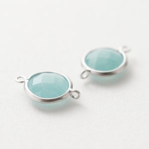May include: Two silver-toned metal connector charms with a light blue gemstone in the center. The charms have a loop on each side for attaching to jewelry.