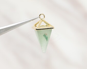 May include: A gold-colored pendant with a geometric design, featuring a light green, triangular gemstone. The pendant is held by tweezers against a white background, showcasing its polished surface and intricate details. The gemstone has a few green inclusions.