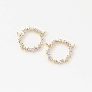 May include: Two gold-toned metal circle charms with a row of clear sparkling rhinestones around the edge. Each charm has a small loop on the top for attaching to jewelry.