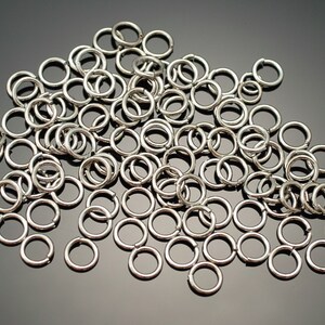 May include: A large pile of silver jump rings, a type of jewelry finding used for connecting chains, cords, and other jewelry components.