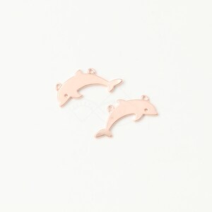 May include: Two rose gold dolphin charms with jump rings. The dolphins are facing the right side of the image.