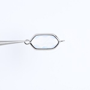 May include: A silver-toned hexagonal charm with a clear glass or crystal insert. The charm has a loop at the top for attaching to a necklace or bracelet.