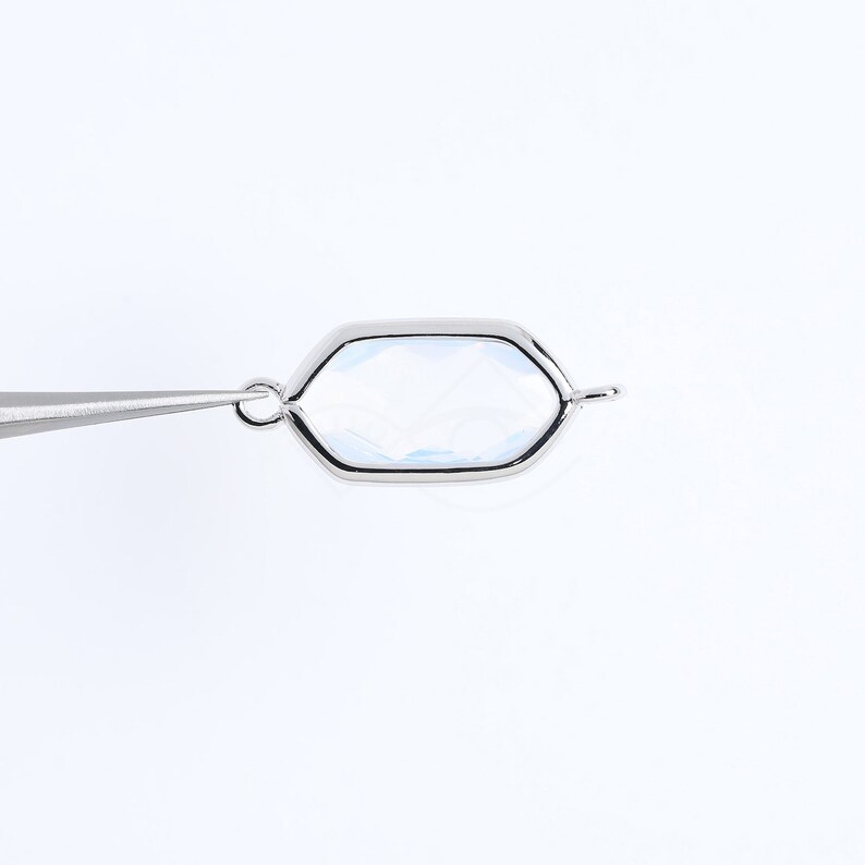 May include: A silver-toned hexagonal charm with a clear glass or crystal insert. The charm has a loop at the top for attaching to a necklace or bracelet.