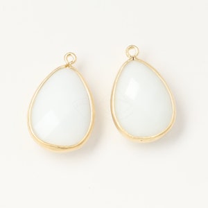 May include: Two white teardrop-shaped glass beads with gold metal frames and loops at the top.