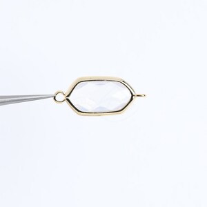 May include: A gold-toned metal pendant with a clear glass octagon-shaped insert. The pendant has a loop at the top for attaching to a chain or cord.