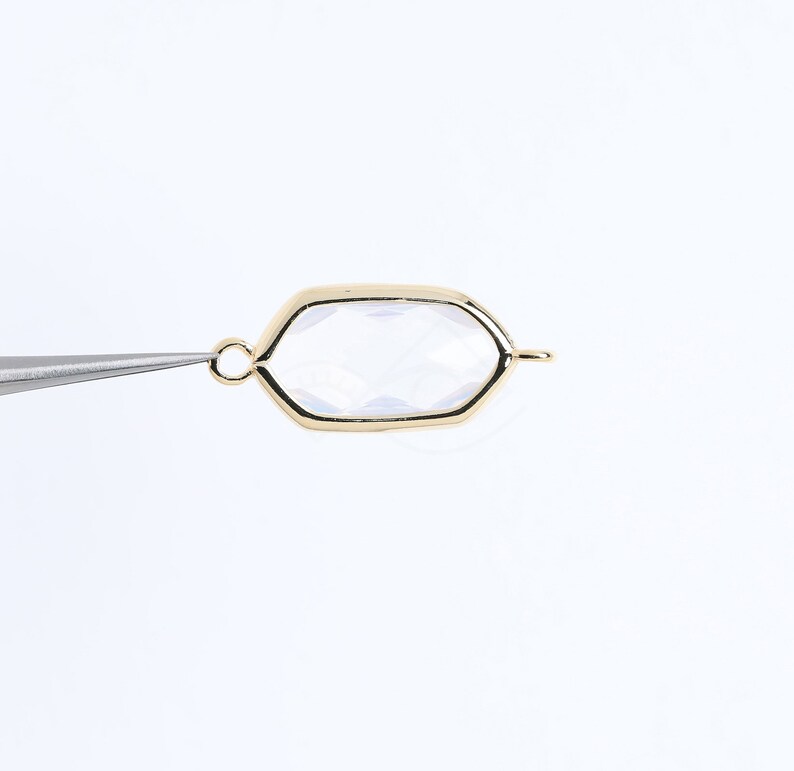 May include: A gold-toned metal pendant with a clear glass octagon-shaped insert. The pendant has a loop at the top for attaching to a chain or cord.