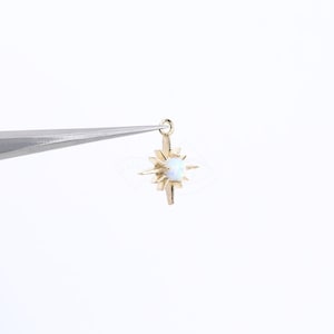 Puede incluir: Encanto de estrella dorada con una opala blanca en el centro. La estrella tiene ocho puntas y está unida a un anillo de salto.