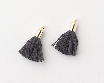 May include: Two gray tassel charms with gold metal tops. The tassels are made of soft, fluffy yarn.