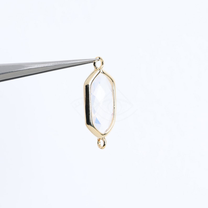 May include: Gold-toned pendant with a clear faceted gemstone. The pendant has two loops for attaching a chain or cord.