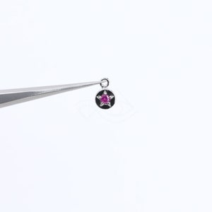 May include: A silver charm with a pink star-shaped gemstone in the center. The charm is round and has a small loop at the top for attaching to a bracelet or necklace.