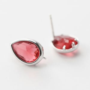 May include: A pair of silver teardrop earrings with red crystal stones.