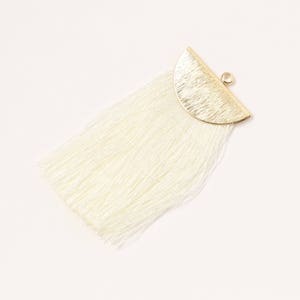 May include: A white tassel earring with a gold half-circle pendant. The pendant has a textured surface.
