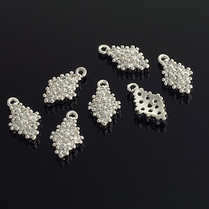 Puede incluir: Siete dijes de plata en forma de diamante con adornos de cristal transparente. Los dijes tienen un bucle en la parte superior para sujetarlos a joyas.