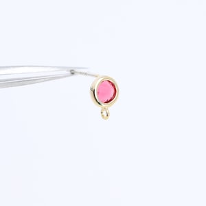 Puede incluir: Pendiente dorado con una piedra redonda de cristal rosa y un pequeño bucle en la parte inferior.