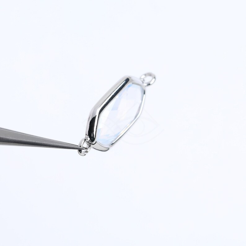 May include: A silver-toned pendant with a clear, faceted gemstone in a hexagonal shape. The pendant has a loop at the top for attaching to a chain.