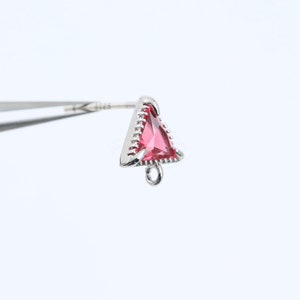 Può includere: Un orecchino triangolare in argento con una pietra preziosa rosa e un anello in basso.