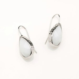 Peut inclure: Une paire de boucles d'oreilles pendantes en argent avec des pierres blanches en forme de larme. Les pierres ont une finition texturée et martelée.
