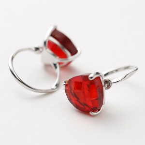 May include: A pair of silver earrings with red gemstone accents. The earrings feature a teardrop-shaped gemstone with a faceted design.
