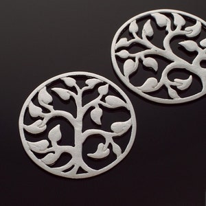 May include: Two silver metal round charms with a tree of life design. The charms are cut out and have a delicate, intricate design.