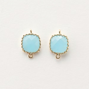 May include: Two light blue square-shaped glass beads with gold-toned metal frames and loops. The beads have a faceted design.