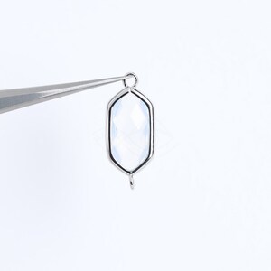 May include: A silver-toned pendant with a clear, faceted gemstone in a hexagonal shape. The pendant has a loop at the top for attaching to a chain or cord.