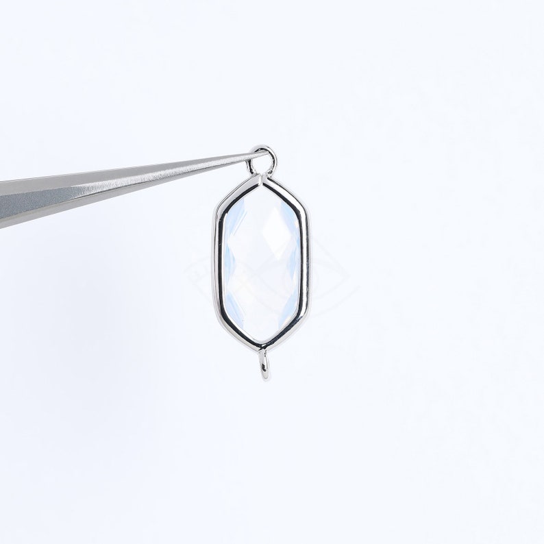 May include: A silver-toned pendant with a clear, faceted gemstone in a hexagonal shape. The pendant has a loop at the top for attaching to a chain or cord.