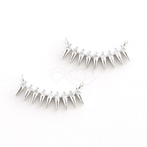 May include: Two silver-toned metal pieces with a row of pointed spikes, each spike topped with a clear rhinestone. The pieces are curved into a slight smile shape.