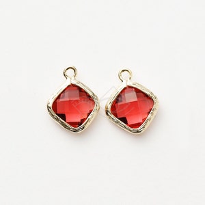 May include: Two gold-toned charms with red square-shaped glass stones. The stones have a faceted design.