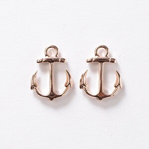 May include: Two rose gold-colored anchor charms. Each charm has a loop at the top for stringing and a classic anchor design. The anchors are displayed on a white background.