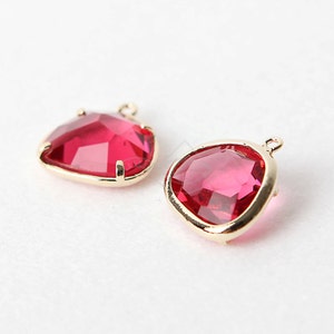 May include: Two gold-toned pendant charms with a red faceted glass stone. The stones are shaped like a heart and a teardrop.