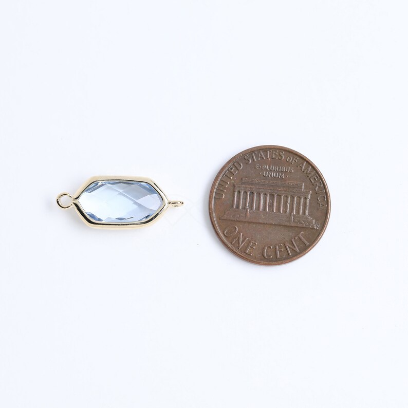 May include: A gold-toned connector with a light blue faceted glass insert. The connector is about the size of a US penny.